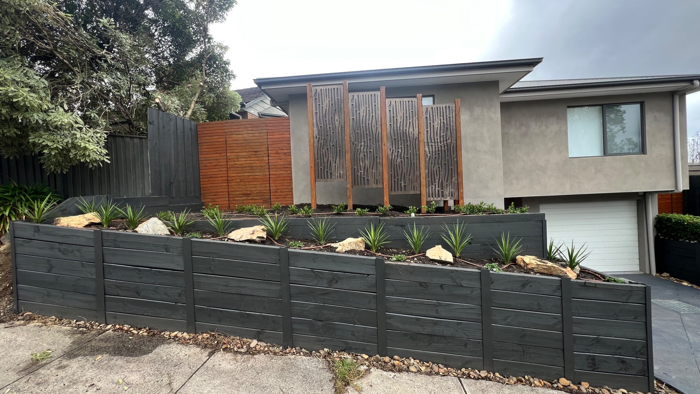 Modern front garden landscape with dark timber retaining walls, planting and real turf installation